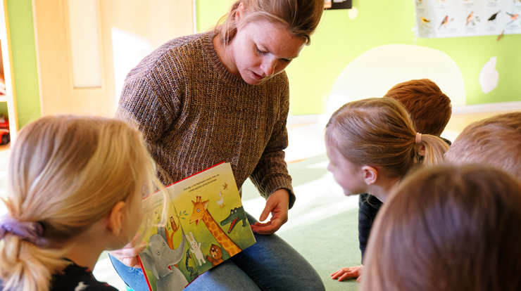 Eine Erzieherin schaut mit mehreren Kindern ein zweisprachiges Buch an.