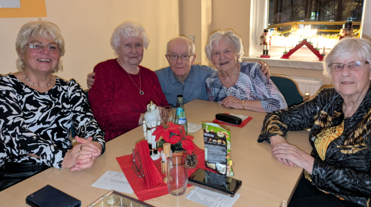 fünf Personen sitzen an einem Tisch und lachen in die Kamera